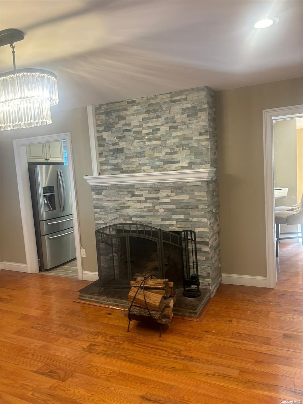 room details featuring a stone fireplace, stainless steel fridge, light hardwood / wood-style floors, and a notable chandelier