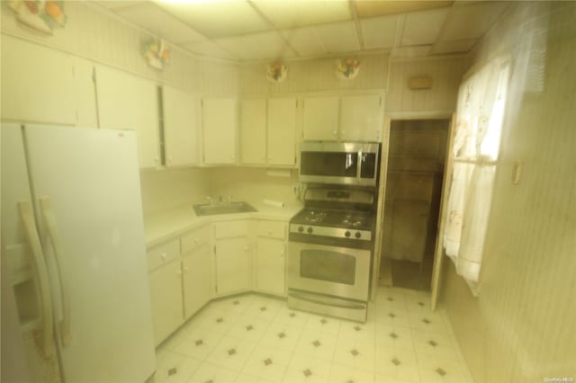 kitchen with white appliances, white cabinetry, a drop ceiling, and sink