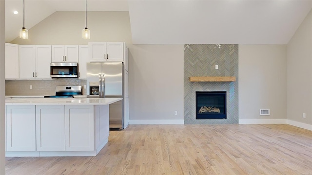 kitchen featuring appliances with stainless steel finishes, decorative backsplash, a fireplace, and white cabinets