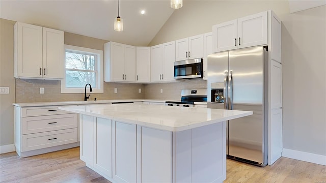 kitchen featuring decorative light fixtures, vaulted ceiling, a kitchen island, stainless steel appliances, and white cabinets