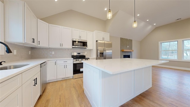 kitchen featuring stainless steel appliances, a center island, vaulted ceiling, white cabinets, and sink