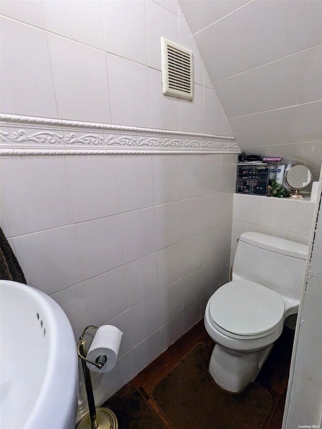 bathroom featuring sink, toilet, lofted ceiling, and tile walls