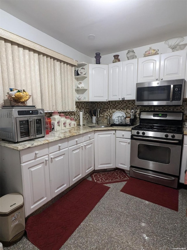 kitchen featuring light stone countertops, sink, backsplash, white cabinets, and appliances with stainless steel finishes