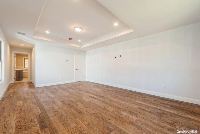 unfurnished room featuring a raised ceiling, wood-type flooring, and ornamental molding