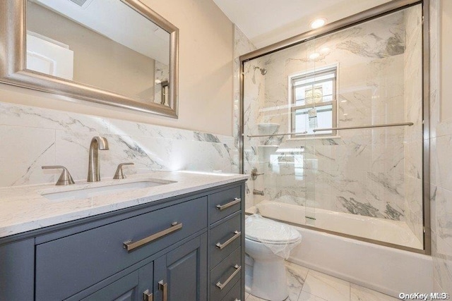 full bathroom with shower / bath combination with glass door, vanity, toilet, and tile walls