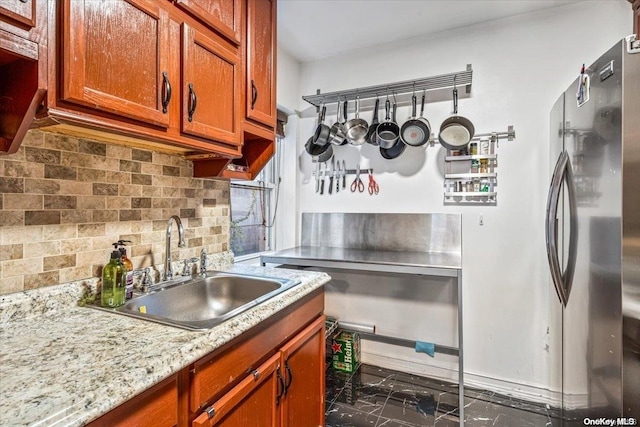 kitchen featuring stainless steel fridge, tasteful backsplash, light stone counters, and sink