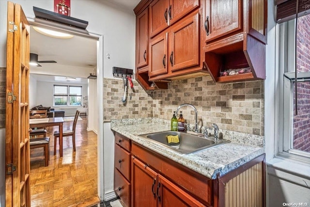 kitchen featuring decorative backsplash, light stone counters, ceiling fan, sink, and light parquet flooring