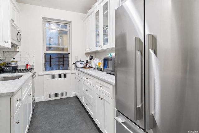 kitchen featuring white cabinets, appliances with stainless steel finishes, light stone counters, and radiator