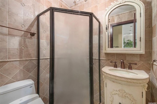 bathroom featuring vanity, toilet, a shower with shower door, and tile walls