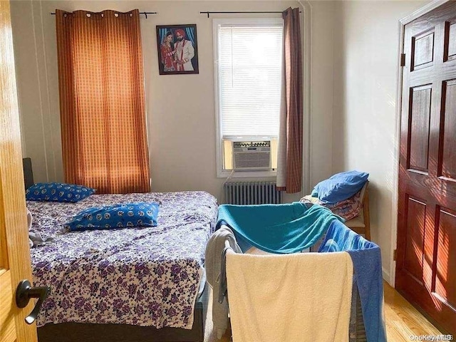 bedroom with radiator heating unit, cooling unit, and wood-type flooring