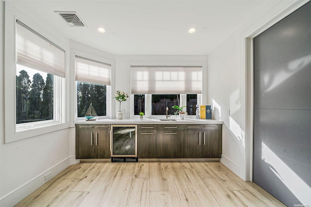 bar featuring light hardwood / wood-style floors, dark brown cabinetry, and beverage cooler