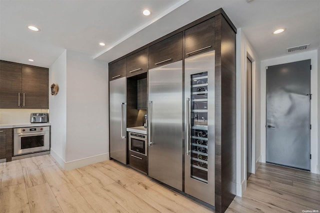 kitchen featuring dark brown cabinets, light hardwood / wood-style floors, and appliances with stainless steel finishes