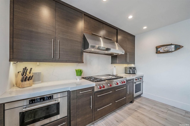 kitchen with dark brown cabinets, light hardwood / wood-style floors, and appliances with stainless steel finishes