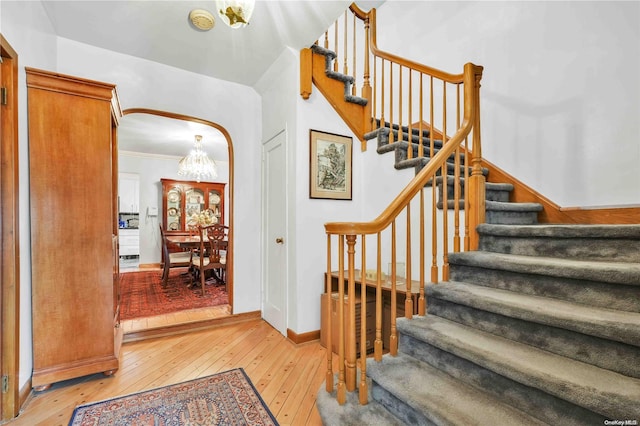 stairs featuring hardwood / wood-style floors, a chandelier, and ornamental molding