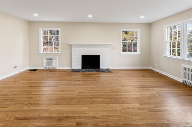 unfurnished living room featuring a brick fireplace, radiator heating unit, and light hardwood / wood-style flooring