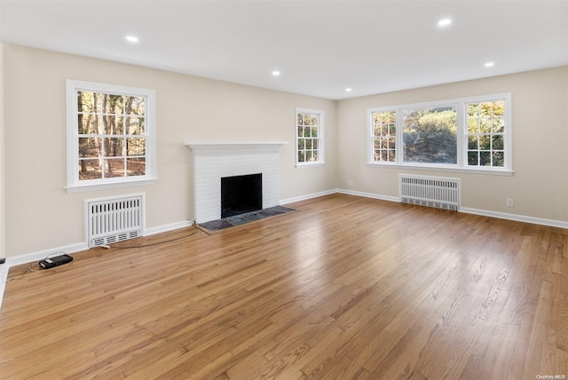 unfurnished living room featuring radiator heating unit, a healthy amount of sunlight, and light hardwood / wood-style flooring