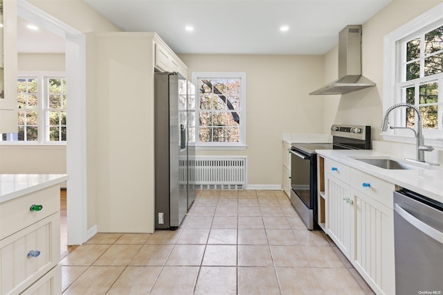 kitchen featuring radiator, stainless steel appliances, sink, wall chimney range hood, and white cabinets