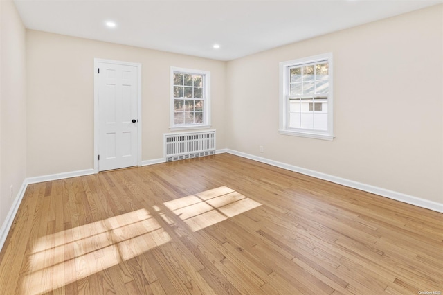 unfurnished room with radiator heating unit, a healthy amount of sunlight, and light hardwood / wood-style floors