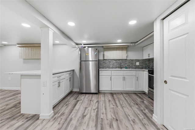 kitchen with white cabinets, light wood-type flooring, kitchen peninsula, and appliances with stainless steel finishes