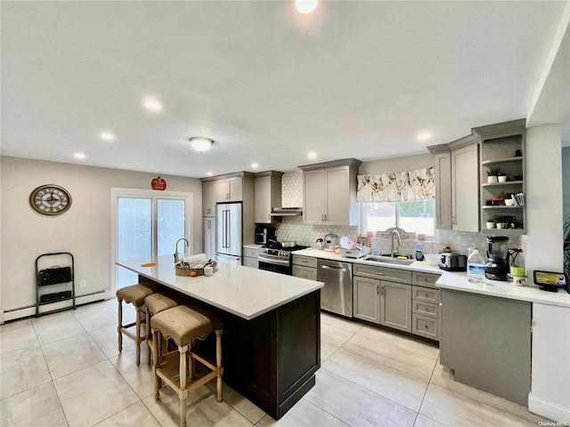 kitchen featuring a breakfast bar, gray cabinets, appliances with stainless steel finishes, a baseboard radiator, and a kitchen island