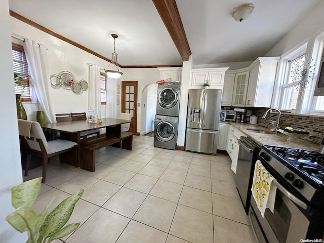 kitchen featuring appliances with stainless steel finishes, white cabinetry, stacked washer / dryer, and sink