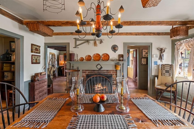 dining space featuring a chandelier, wood-type flooring, a brick fireplace, and beamed ceiling