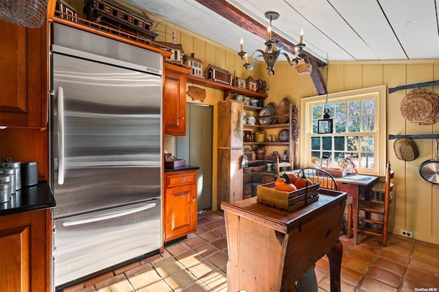 kitchen with hanging light fixtures, stainless steel built in refrigerator, wood walls, vaulted ceiling, and light tile patterned floors