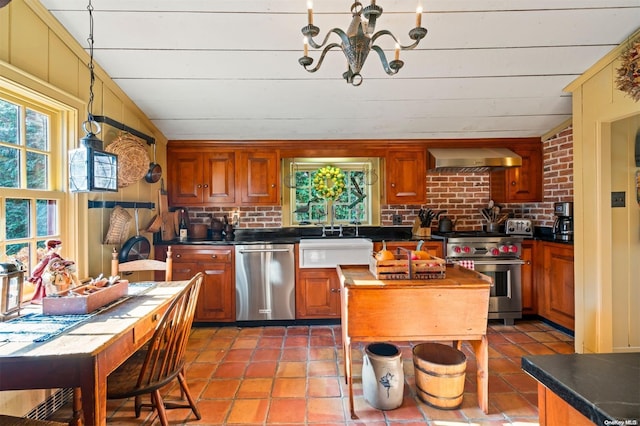 kitchen with sink, wall chimney exhaust hood, appliances with stainless steel finishes, tasteful backsplash, and a notable chandelier