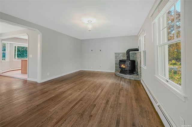 unfurnished living room with a wood stove, dark hardwood / wood-style floors, a baseboard radiator, and a wealth of natural light