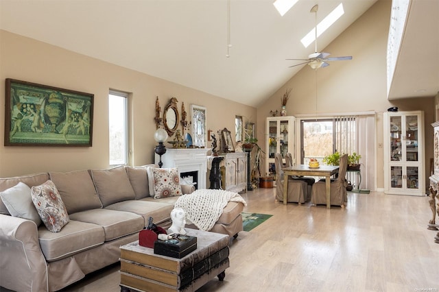 living room with a skylight, ceiling fan, light hardwood / wood-style flooring, and high vaulted ceiling