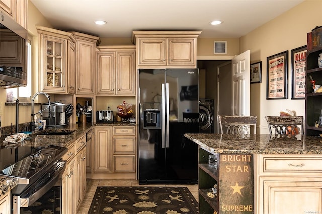 kitchen with appliances with stainless steel finishes, sink, light tile patterned floors, dark stone countertops, and washer / dryer