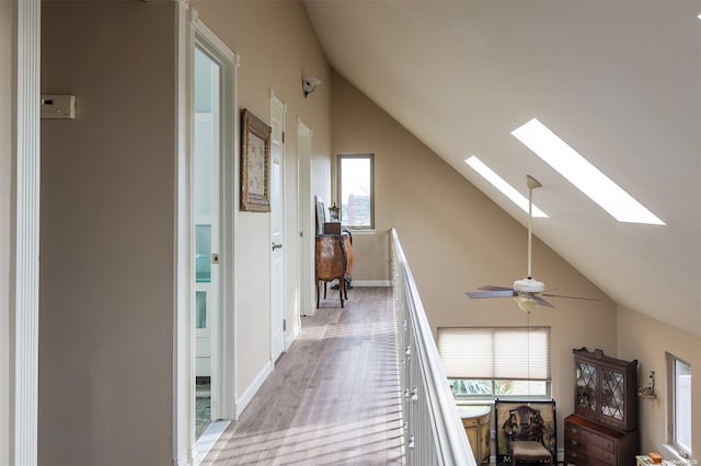 corridor with a skylight, light hardwood / wood-style flooring, and high vaulted ceiling