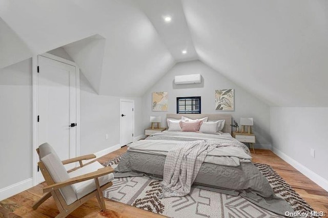 bedroom with a wall unit AC, wood-type flooring, and vaulted ceiling