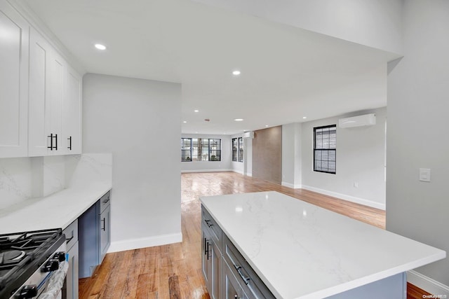 kitchen featuring light wood-type flooring, light stone counters, a wall unit AC, a kitchen island, and white cabinetry