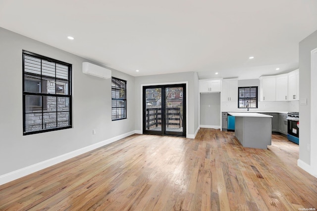 kitchen with stainless steel range with gas cooktop, light wood-type flooring, a wall mounted AC, a kitchen island, and white cabinetry