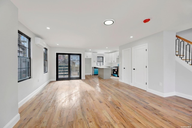 unfurnished living room featuring a wall mounted air conditioner and light hardwood / wood-style floors