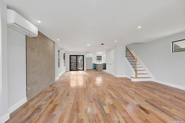 unfurnished living room featuring a wall mounted AC, light hardwood / wood-style flooring, and french doors