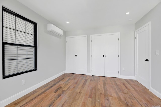 unfurnished bedroom featuring a wall mounted air conditioner, light hardwood / wood-style flooring, and multiple closets