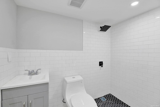 bathroom with tiled shower, toilet, tile walls, and vanity