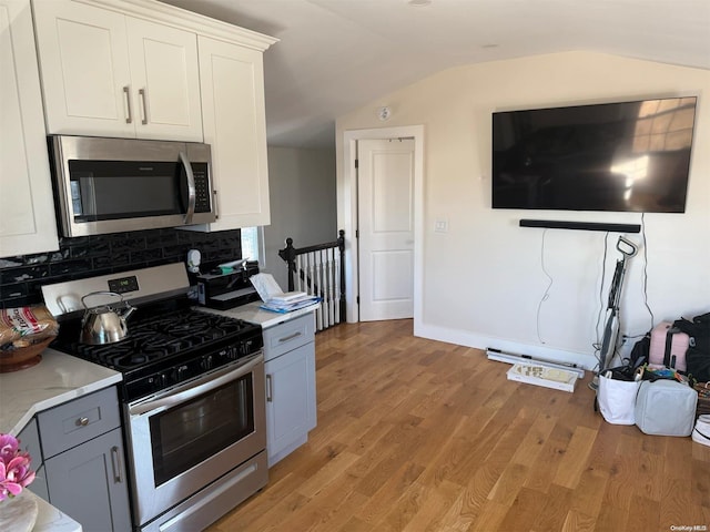 kitchen with gray cabinetry, white cabinetry, light hardwood / wood-style floors, lofted ceiling, and appliances with stainless steel finishes