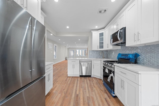 kitchen with light stone countertops, tasteful backsplash, appliances with stainless steel finishes, white cabinets, and light wood-type flooring