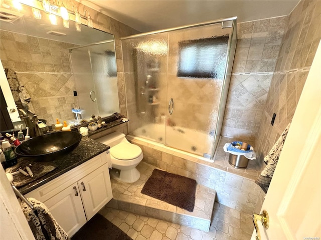 full bathroom featuring toilet, tile walls, tile patterned flooring, shower / bath combination with glass door, and vanity