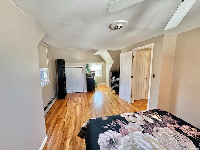 bedroom featuring light hardwood / wood-style flooring, baseboard heating, and lofted ceiling