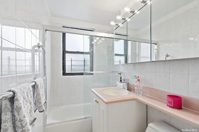 full bathroom with vanity, combined bath / shower with glass door, decorative backsplash, toilet, and tile walls