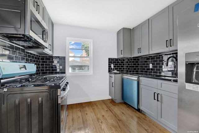 kitchen featuring gray cabinetry, sink, stainless steel appliances, tasteful backsplash, and light hardwood / wood-style flooring