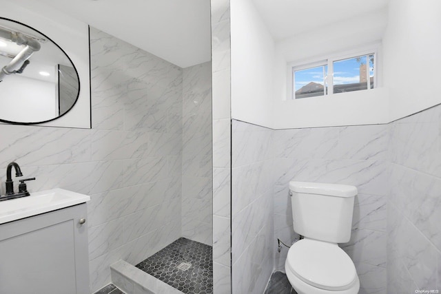 bathroom featuring a tile shower, vanity, toilet, and tile walls