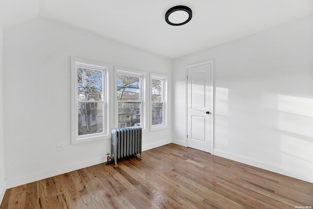 spare room featuring light wood-type flooring, vaulted ceiling, and radiator