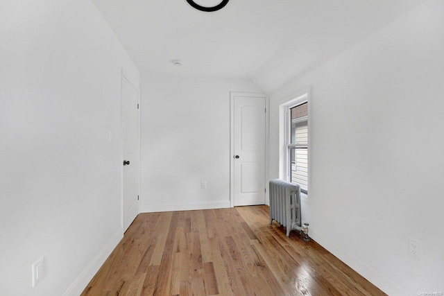 empty room with radiator heating unit, vaulted ceiling, and light hardwood / wood-style flooring