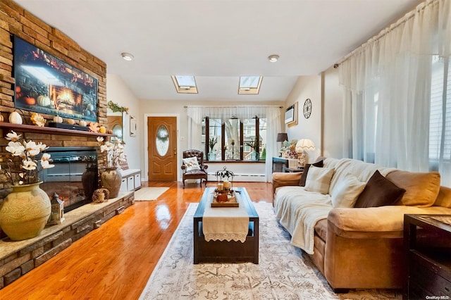 living room featuring a stone fireplace, vaulted ceiling with skylight, and light hardwood / wood-style floors