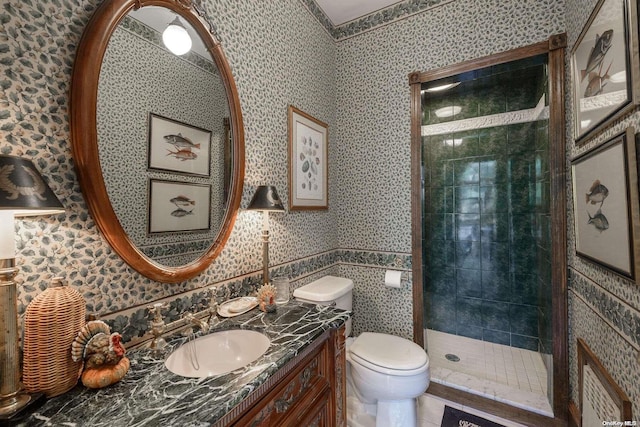 bathroom with toilet, a tile shower, and vanity